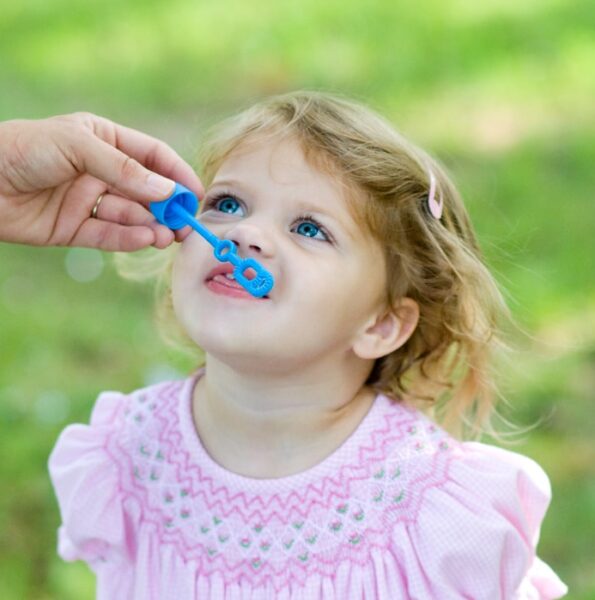 person hand holding bubble maker toy near toddler's mouth