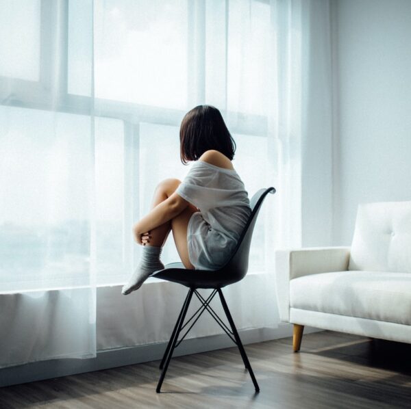 woman sitting on black chair in front of glass-panel window with white curtains