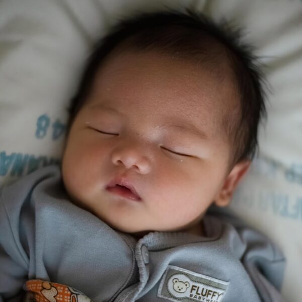 baby in gray onesie lying on bed