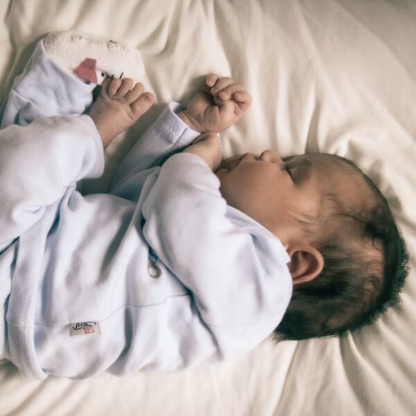 baby in blue blanket sleeper lying on bed