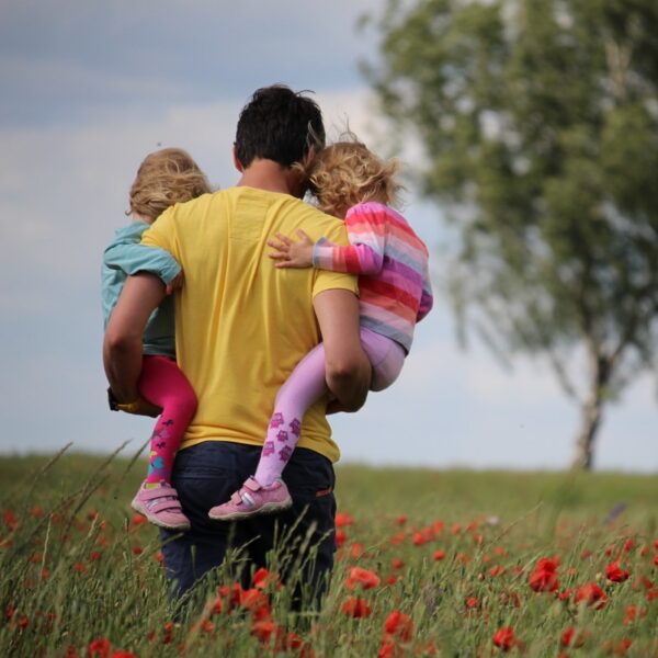 man carrying to girls on field of red petaled flower