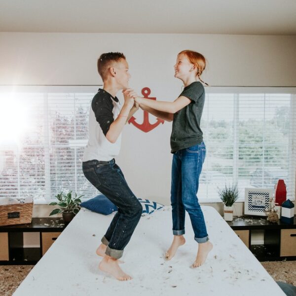 boy and girl jumping on white bed mattress inside room