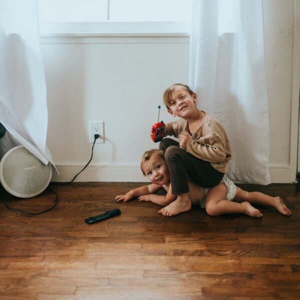 woman in brown long sleeve shirt sitting on floor with baby in white long sleeve shirt