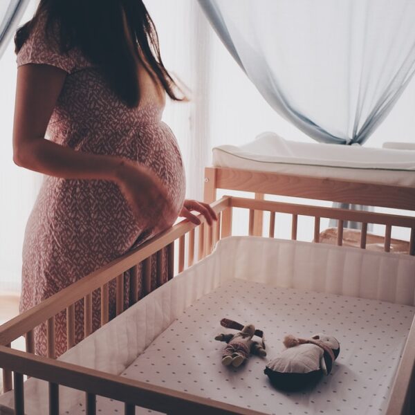 woman in white lace sleeveless dress standing beside brown wooden crib