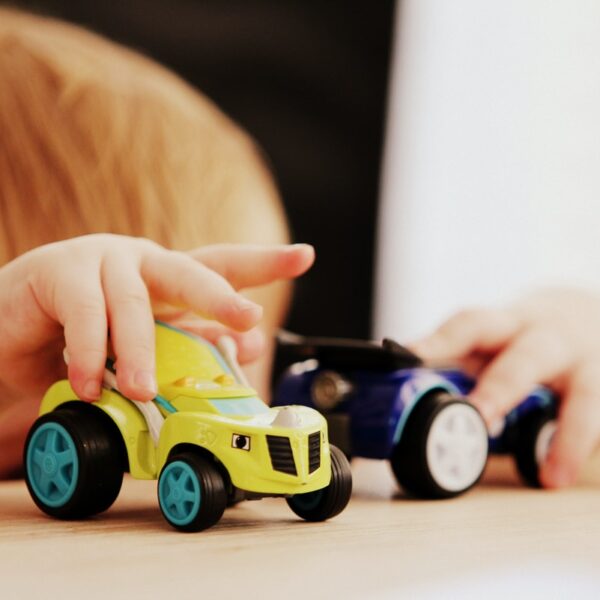 child playing with two assorted-color car plastic toys on brown wooden table