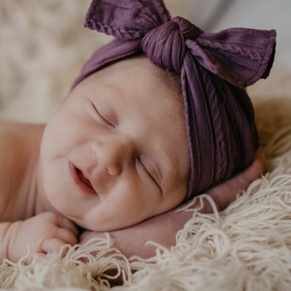 baby in purple knit cap lying on white fur textile