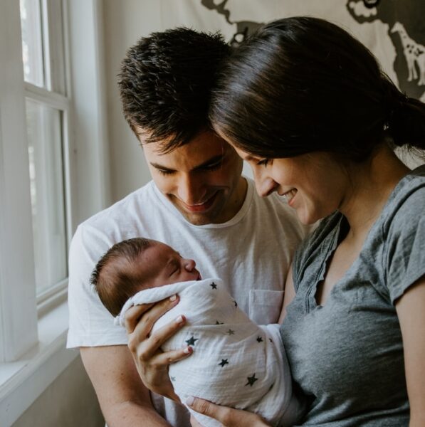 woman holding baby beside man smiling