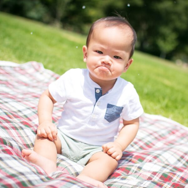 selective focus photography of grumpy face toddler sitting on plaid pad taken during daytime