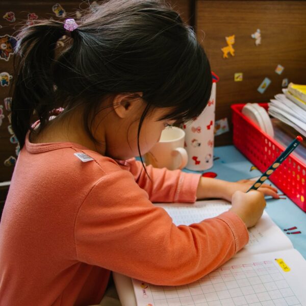 girl in pink long sleeve shirt writing on white paper