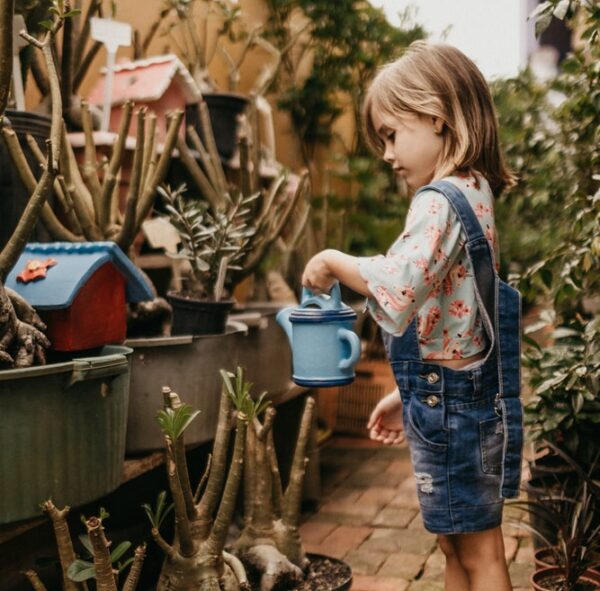 girl wearing blue romper holding teal watering can